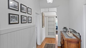 A hallway with white wainscoting, a patterned rug, and a wooden dresser with decorative items.