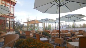 An outdoor seating area with wicker chairs and tables, umbrellas, and a building in the background.