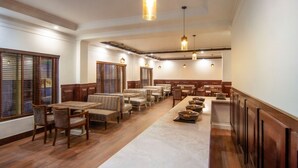 A spacious restaurant with wooden flooring, multiple seating areas including a long communal table, and pendant lighting.