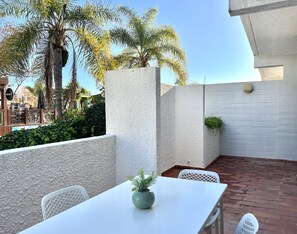 Eine Terrasse mit einem weißen Tisch und Stühlen, einem Topfpflanzen und im Hintergrund eine Aussicht auf Palmen und Gebäude.