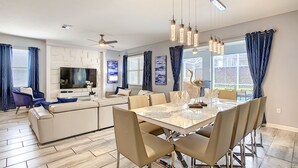 A modern living room with a large TV, sofa, and dining table with chairs. - 8BR • Arcade & Game Room • 2 Theaters • Pool & Spa (Davenport)