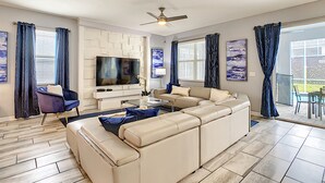 A modern living room with a sectional sofa, a flat-screen TV, and a ceiling fan. - 8BR • Arcade & Game Room • 2 Theaters • Pool & Spa (Davenport)