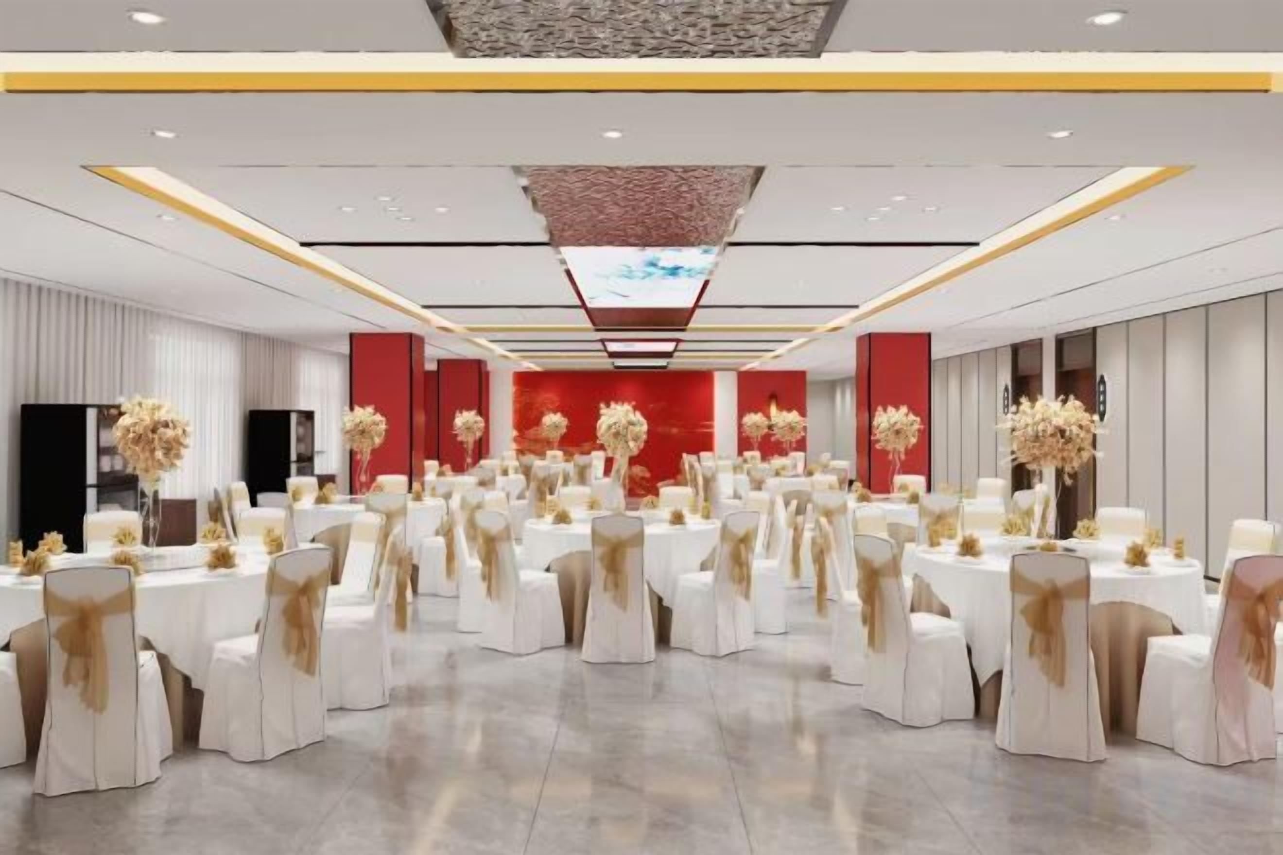 A large banquet hall with round tables and chairs, red accent walls, and floral centerpieces.