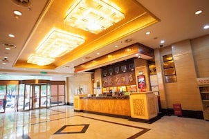 A hotel lobby with a reception desk, a glass door entrance, and a ceiling with recessed lighting.