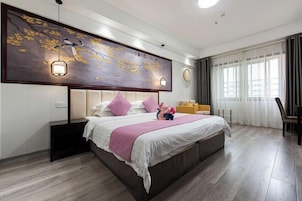 Una habitación de hotel moderna con una cama grande, cabecera con iluminación integrada, un adorno en la pared y una ventana con cortinas.