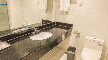 A bathroom with a black countertop sink, a mirror, a toilet, and a trash bin.