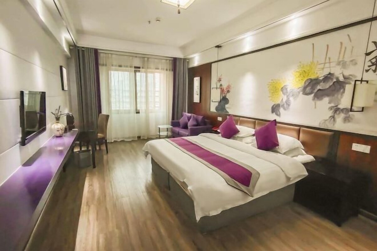 A hotel room with a bed, a desk, a chair, a TV, and a painting on the wall.