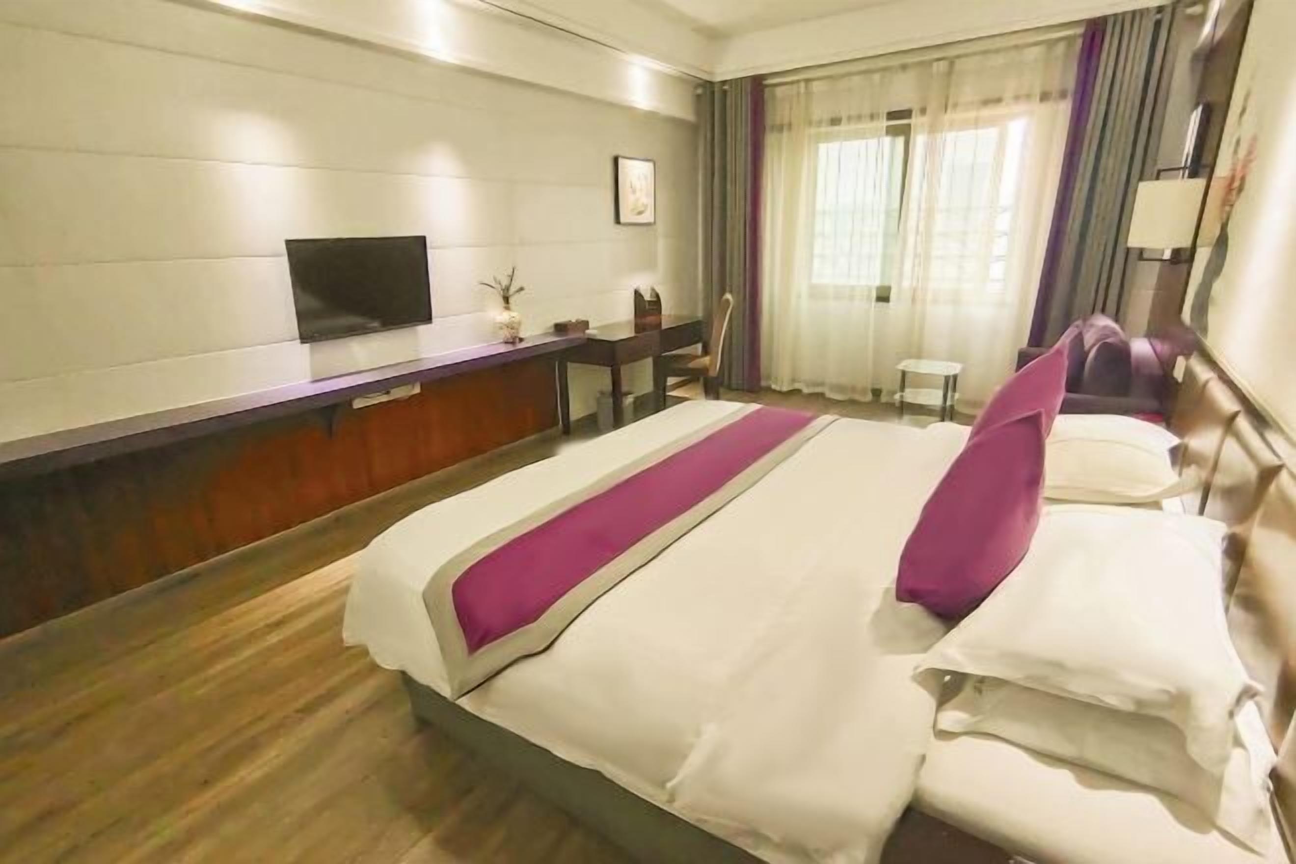 A hotel room with a bed, a desk, a TV, and a window with curtains.
