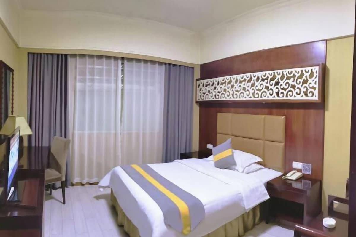 A hotel room with a bed, a desk, a chair, a TV, and a decorative wall panel.