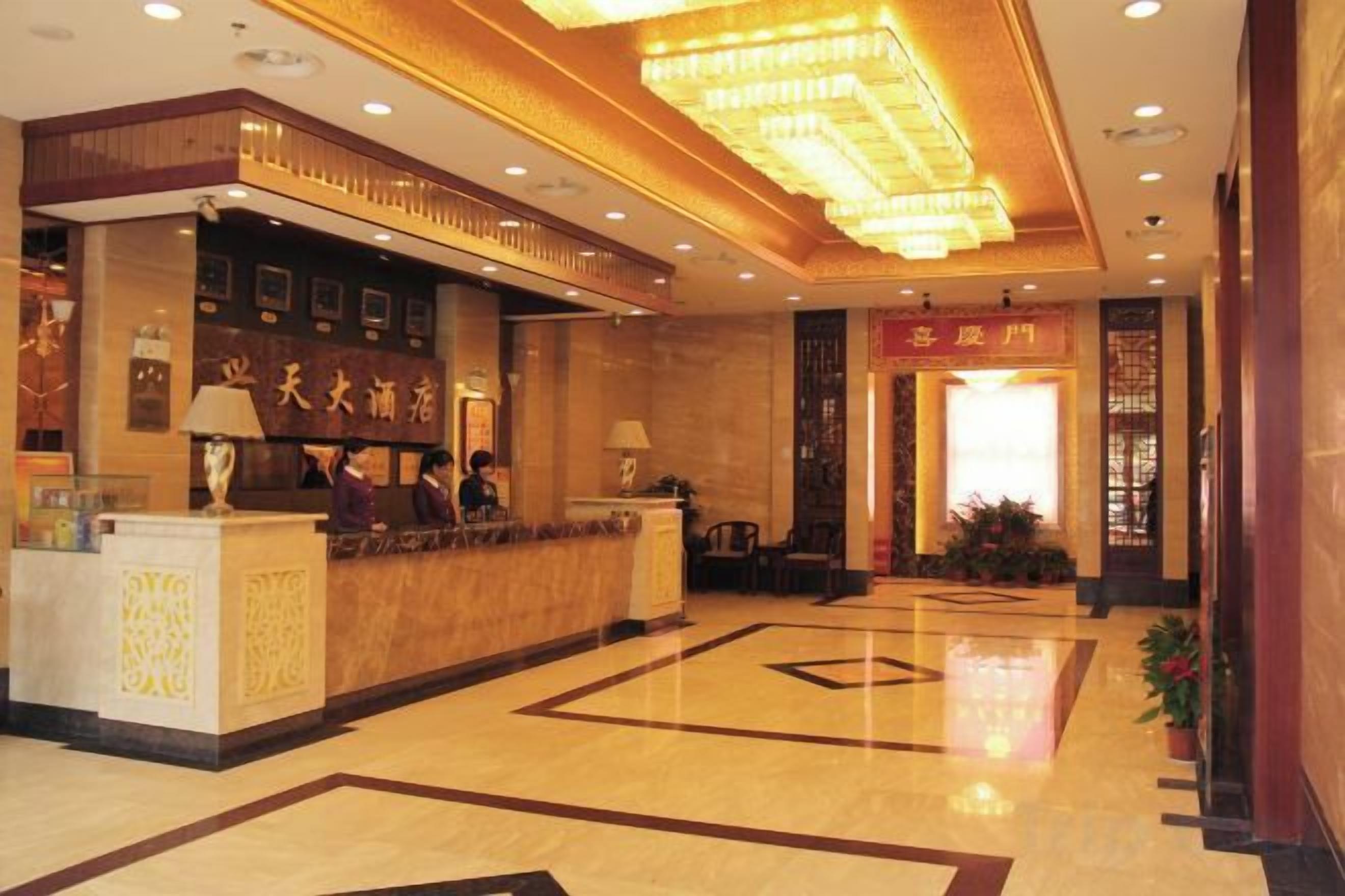 Un vestíbulo de hotel con mostrador de recepción, una gran araña y un piso limpio y pulido.