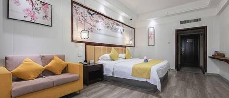 Habitación de hotel con cama, sofá y mesita de noche. Se observan obras de arte enmarcadas en las paredes y una puerta a la derecha.