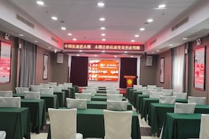 A conference room with rows of tables and chairs, a presentation screen, and a banner with text. - Xingtian Hotel (Yueyang)