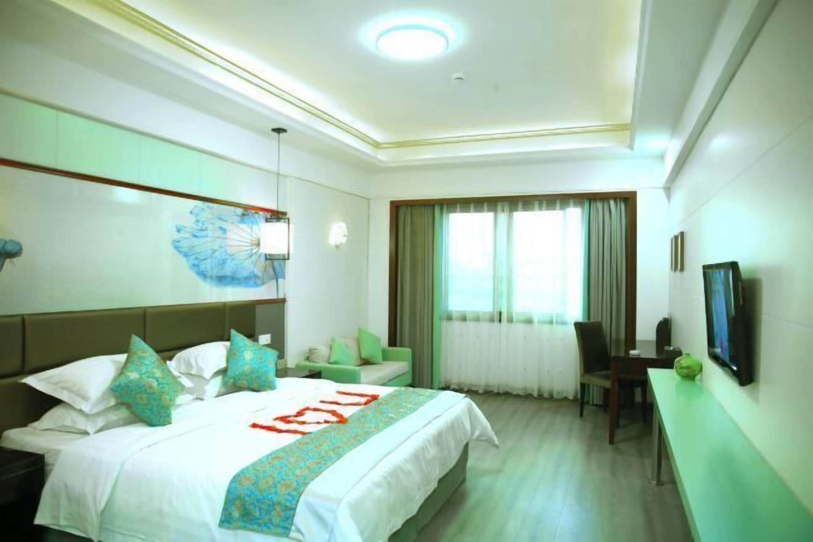 Una habitación de hotel con cama, escritorio, silla, televisor y ventana con cortinas.
