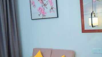 A room with a light blue wall, a framed floral artwork, a mirror with a light fixture, and a sofa with yellow and pink cushions.