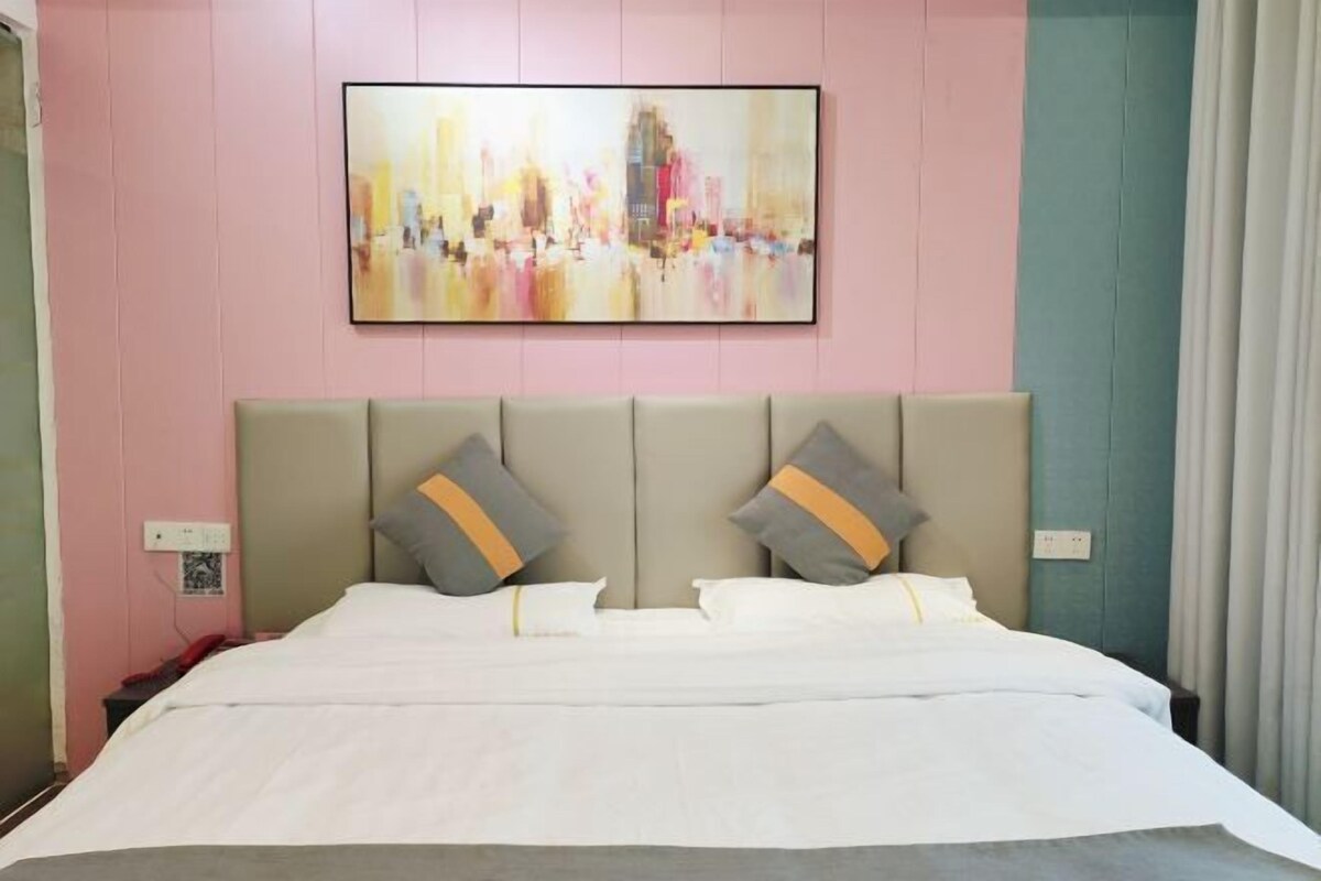 A hotel room with a large bed, two pillows, a headboard, and a cityscape painting on the wall.