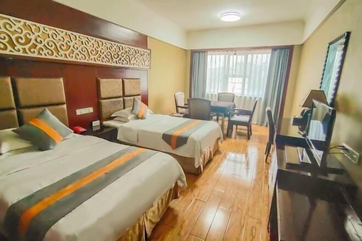 A hotel room with two beds, a desk, a chair, a television, and a window with curtains.