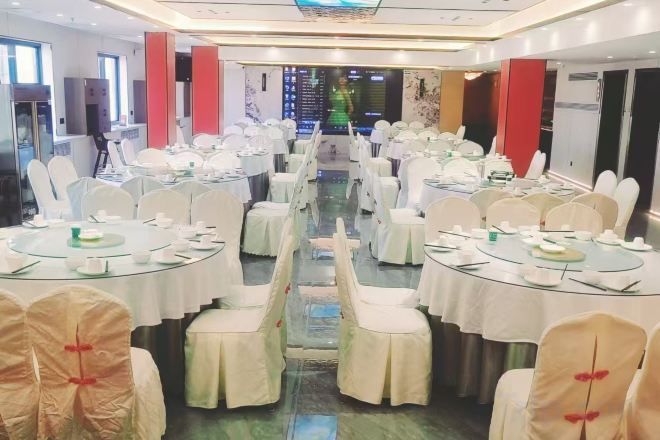 Salão de banquetes com mesas redondas, cadeiras brancas e uma passagem central.