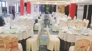 Salão de banquetes com mesas redondas, cadeiras brancas e uma passagem central.