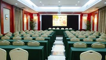 A conference room with rows of tables and chairs, a stage with a projector screen, and a red accent wall.