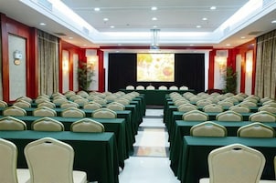A conference room with rows of tables and chairs, a stage with a projector screen, and a red accent wall.