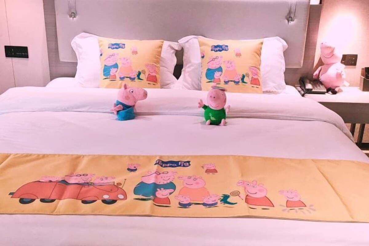 A hotel room with a bed featuring Peppa Pig-themed bedding and pillows.