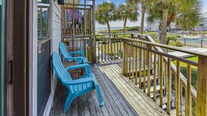 A wooden deck with blue chairs, a railing, and a view of palm trees and a pool.