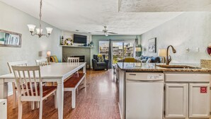 A spacious kitchen with a central island, a dining area with white chairs, a fireplace, and a television mounted above it.