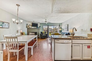 A spacious kitchen with a central island, a dining area with white chairs, a fireplace, and a television mounted above it.