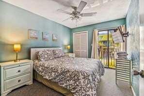 A bedroom with a bed, bedside lamps, a ceiling fan, and a view of the outside.