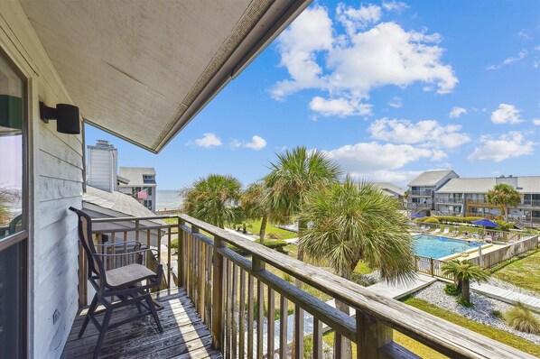 A balcony with a view of a swimming pool and palm trees.