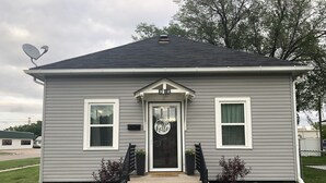 A single-story house with a front door, two windows, a satellite dish, and a small porch area. - Updated kitchen, Close to downtown, Pet friendly, Privacy fenced backyard! (Kearney)