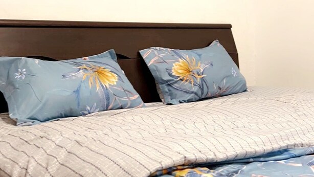 A bedroom with a bed, two pillows with floral designs, and a painting of a sunset on the wall. - Freedom 2 furnished room (Dakar)