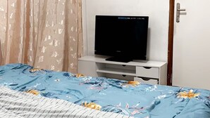 A bedroom with a bed, a TV on a stand, an air conditioner, and a door. - Freedom 2 furnished room (Dakar)