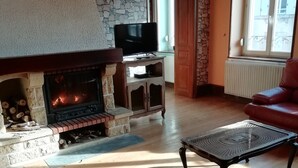 Un salon avec une cheminée en pierre, un téléviseur posé sur un meuble, un canapé en cuir et une table basse à motifs.