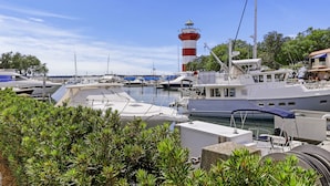 Ein Yachthafen mit vertäuten Booten, ein Leuchtturm im Hintergrund und üppiges Grün im Vordergrund.