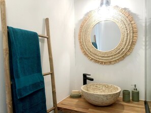 A bathroom with a wooden ladder, a blue towel, a round woven mirror, a stone sink, and a black faucet. - CARIBBEAN CHAMBER (Les Trois-Îlets)