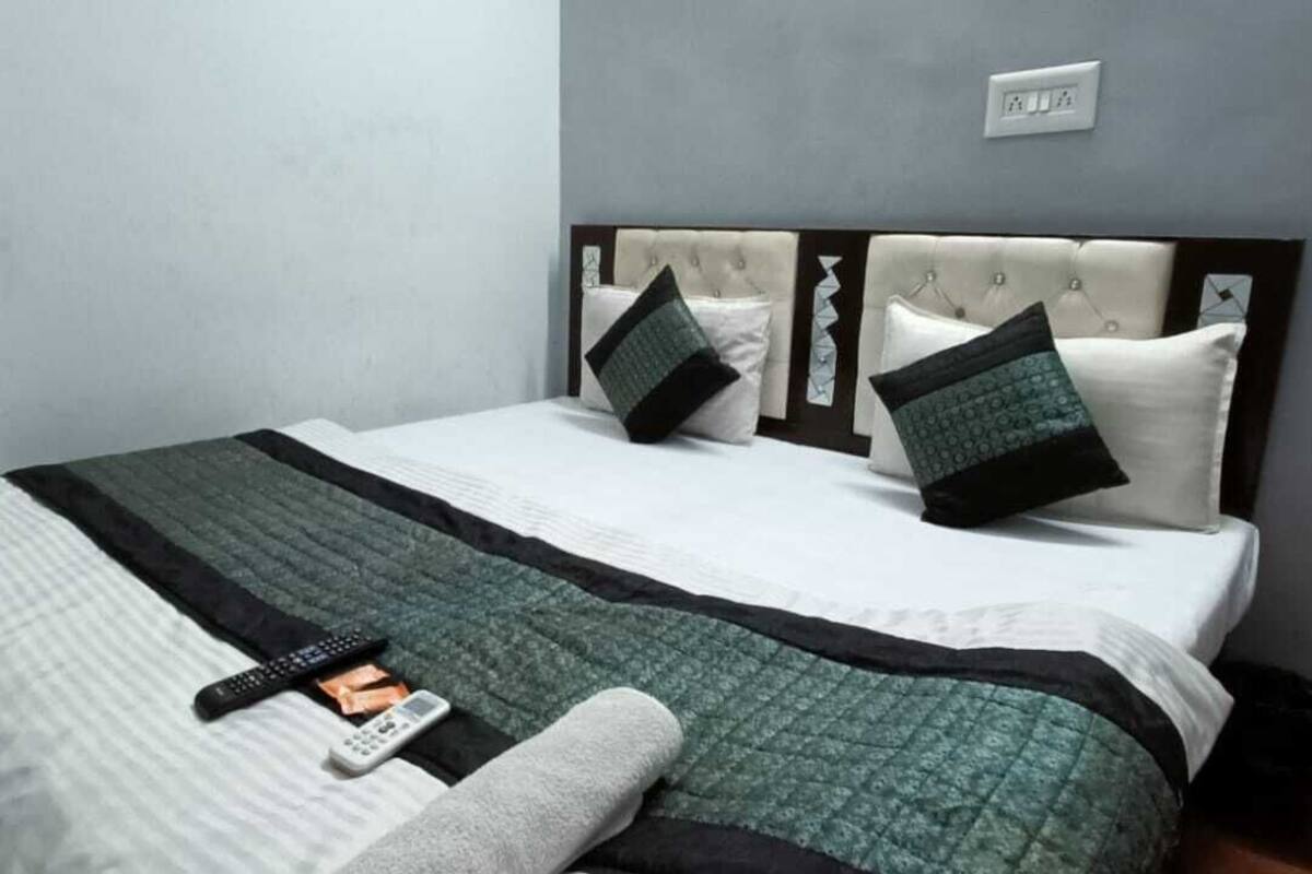 A neatly made bed with a white and green quilt, a remote control, and a smartphone on the bed.