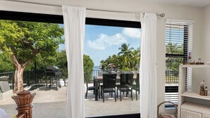 A room with a sliding glass door leading to an outdoor patio with a table and chairs, a grill, and a view of the ocean. - Blue Water is Calling! 5bedroom 3bath with large pool and 150 ft of dockage 2 kayaks included (Marathon)