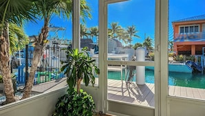 Quarto com vista para uma piscina, palmeiras e um edifício do outro lado da água.