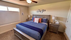 A bedroom with a large bed, two nightstands, a ceiling fan, and a window with blinds.