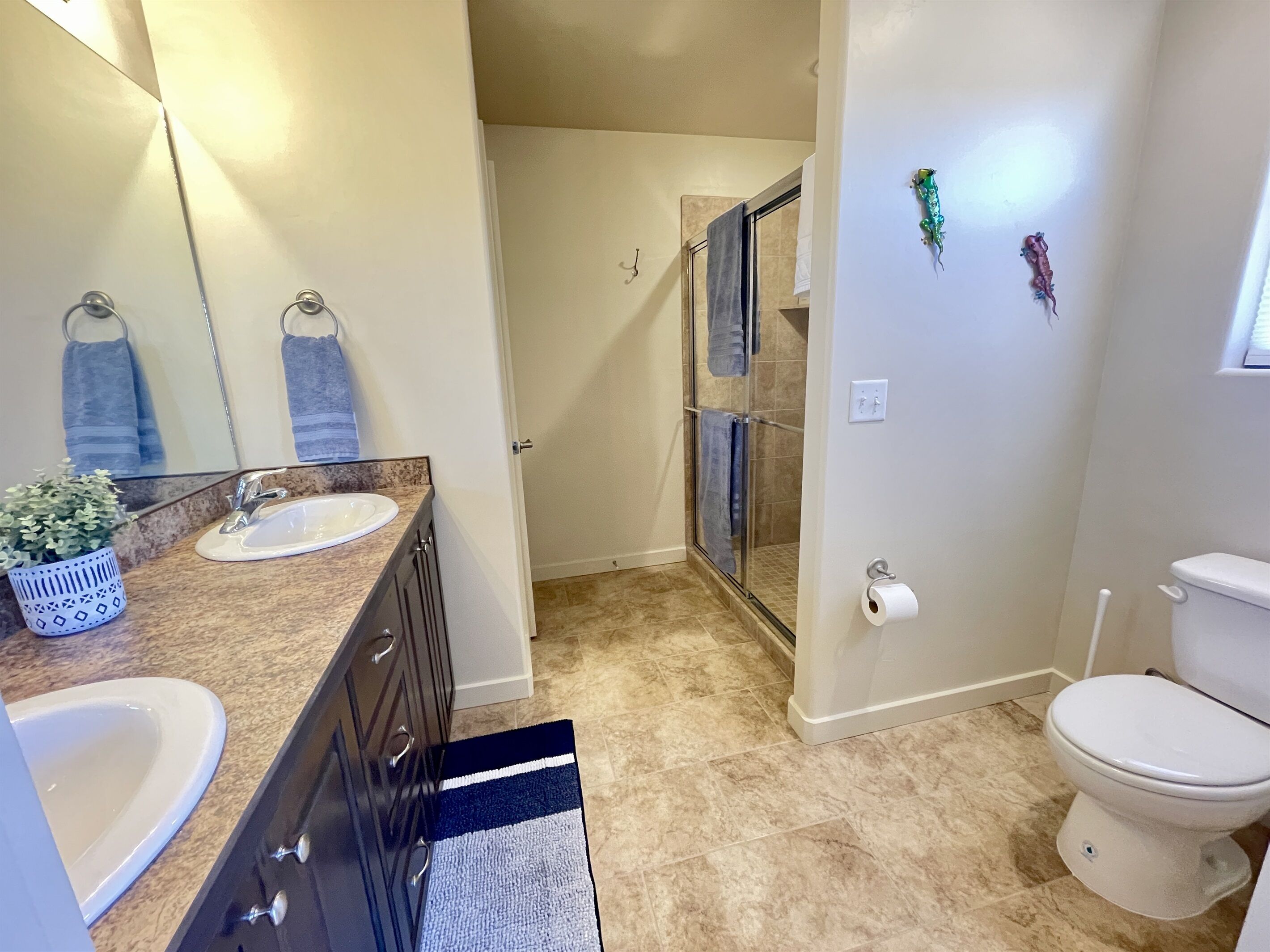 A bathroom with a sink, mirror, and toilet. There is a shower area with a glass door and a towel rack with blue towels.