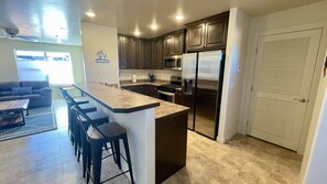 A modern kitchen with dark cabinets, stainless steel appliances, and a bar area with stools.