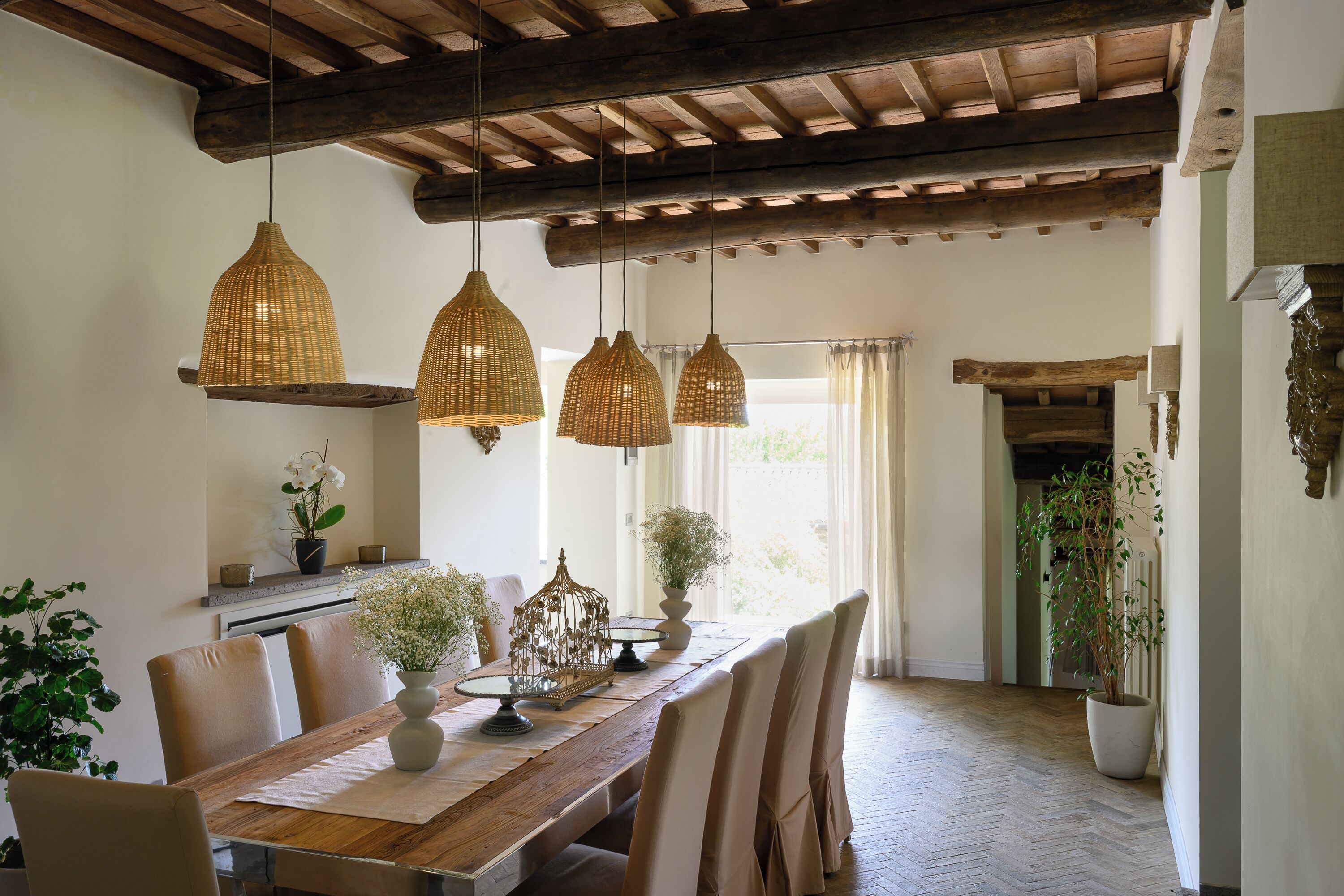 A dining area with a wooden table, chairs, hanging wicker pendant lights, and potted plants.