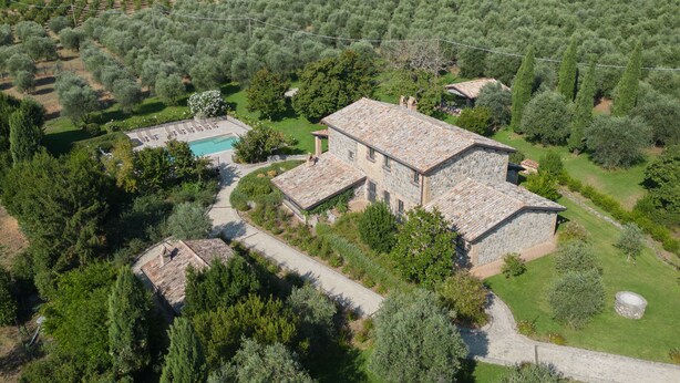 Una villa de piedra con piscina, rodeada de olivos y vegetación.