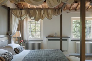 Une chambre à coucher avec un lit, des rideaux, une table de chevet, une lampe et une fenêtre.