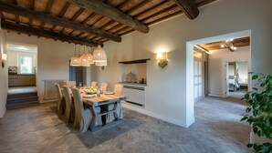 Un comedor espacioso con una mesa y sillas de madera, una cocina al fondo y una escalera que sube a otro nivel.