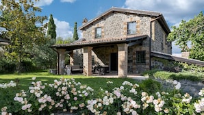 Una casa de piedra con porche cubierto y un jardín de rosas.