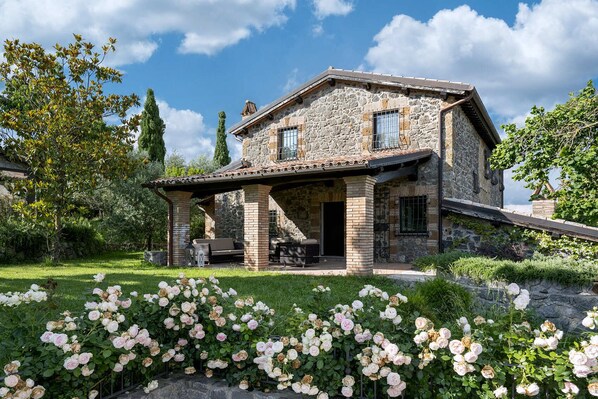 Ein Steinhaus mit überdachter Terrasse und einem Rosengarten.