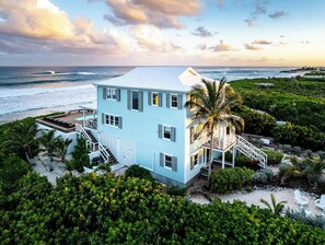 Una casa de dos pisos en tonos azul claro con un balcón, situada en una playa con vistas al océano.