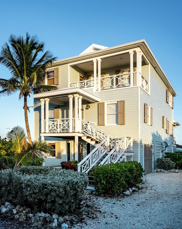 A two-story house with a balcony, a staircase, and a gravel driveway.